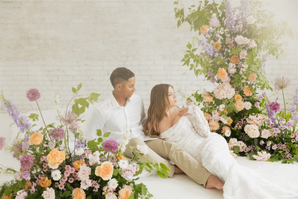 bride and groom posing in a white studio with bright wedding flowers and bouquet