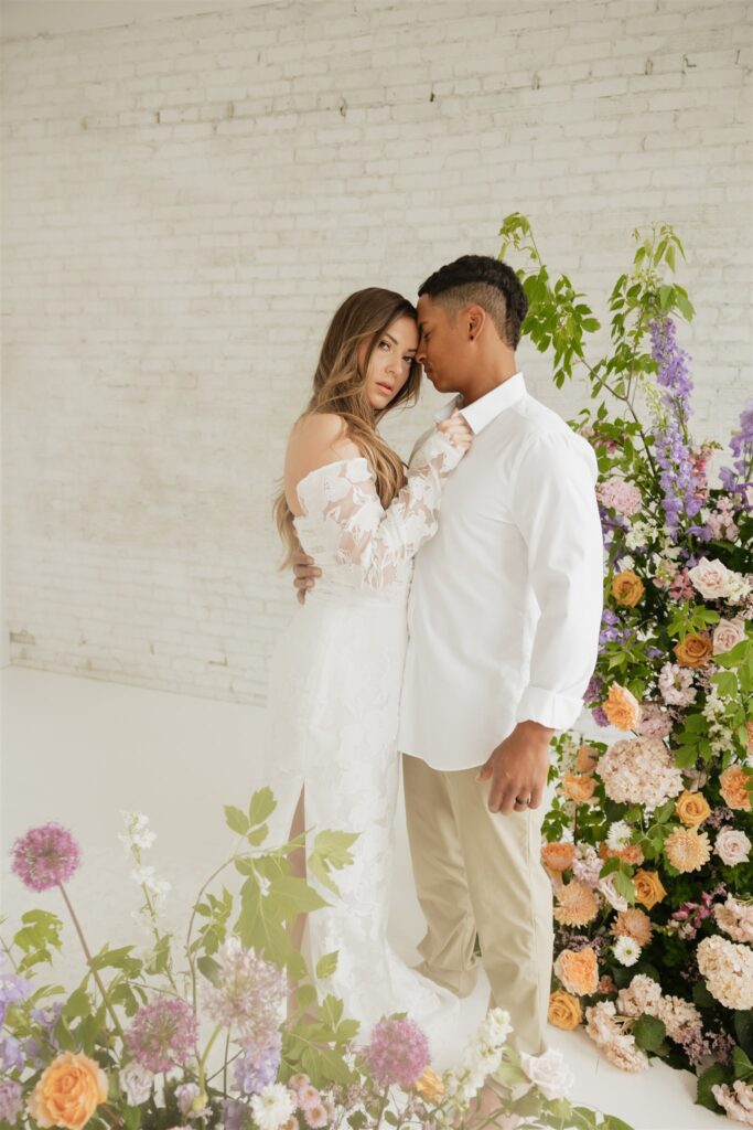 bride and groom posing in a white studio with bright wedding flowers and bouquet
