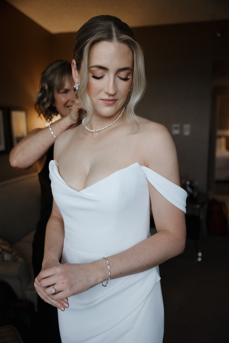 Bride getting ready at Sheraton Cavalier Saskatoon Hotel, wearing a timeless Alyssa Kristin wedding dress, with natural glam by Free Bird Hair Design