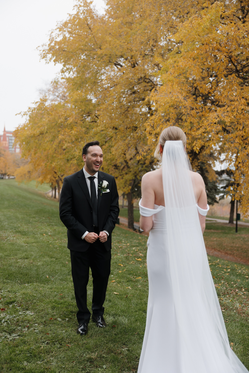 Bride and groom sharing a private first look along the South Saskatchewan River, surrounded by vibrant fall leaves for their timeless, elegant Saskatoon wedding.”
