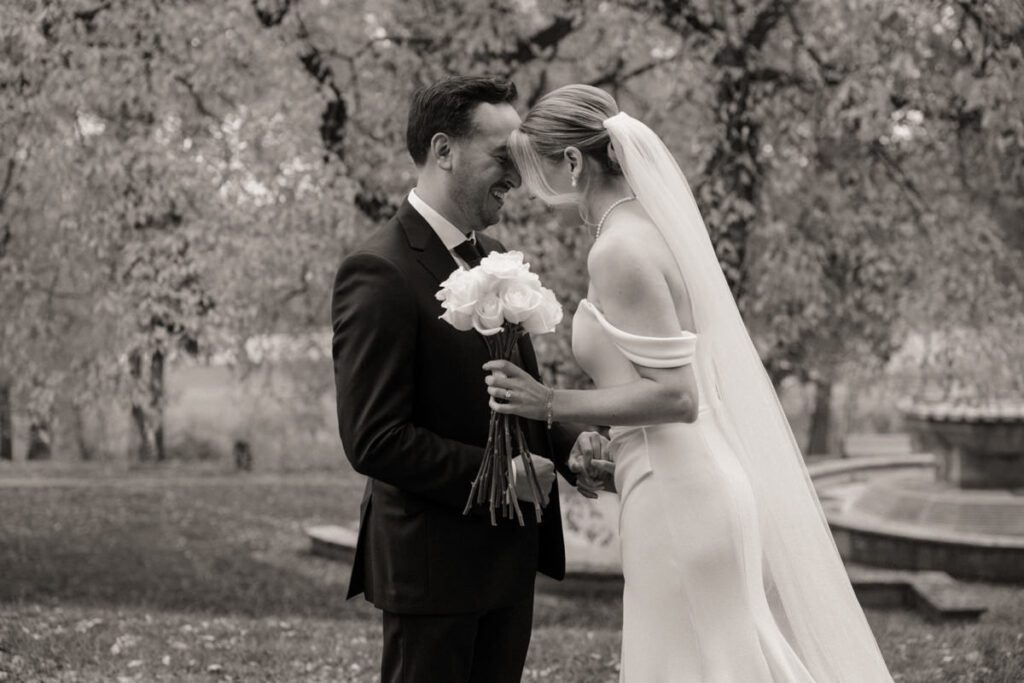 Bride and groom holding hands while exchanging personal vows in a peaceful outdoor setting, surrounded by vibrant autumn leaves.