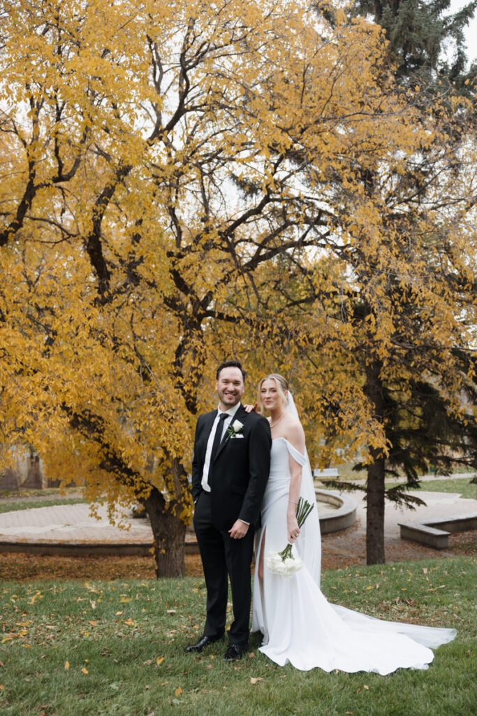Romantic wedding portraits along Saskatoon’s scenic riverbank, with the couple framed by vibrant fall foliage