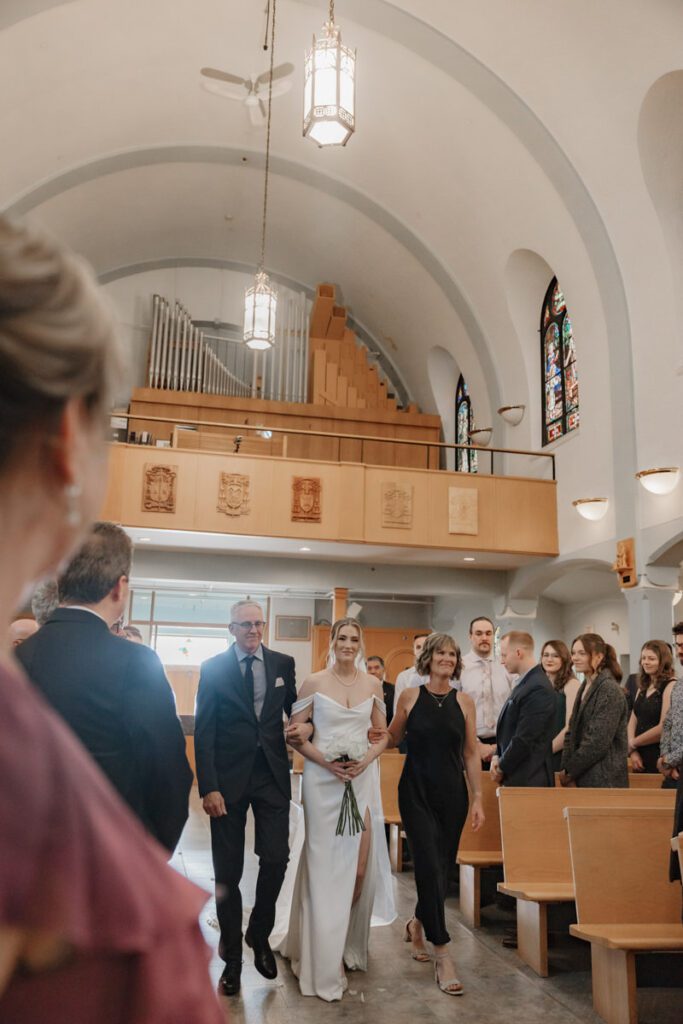 Bride walking down the aisle at St. Paul’s Cathedral, surrounded by classic architecture during a timeless, elegant wedding in Saskatoon.