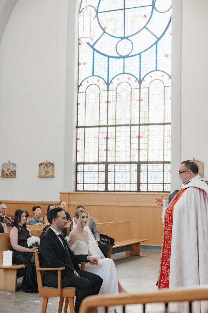 Couple holding hands at the altar during their formal church ceremony, framed by floral arrangements and soft candlelight.