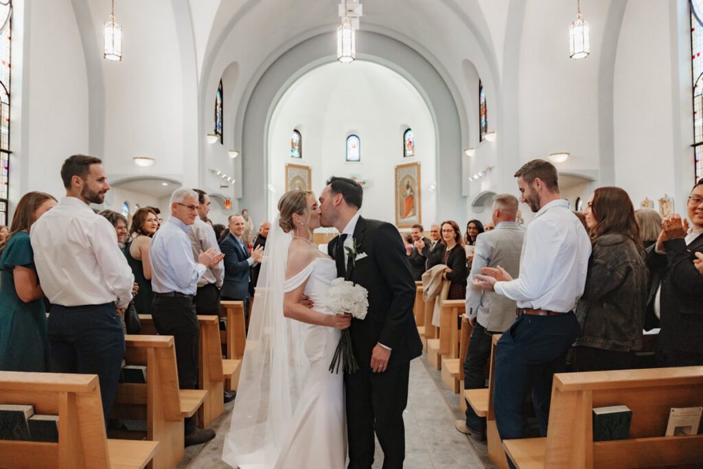 Newlyweds walking up the aisle hand-in-hand after their ceremony, beaming with joy during their timeless Saskatoon wedding