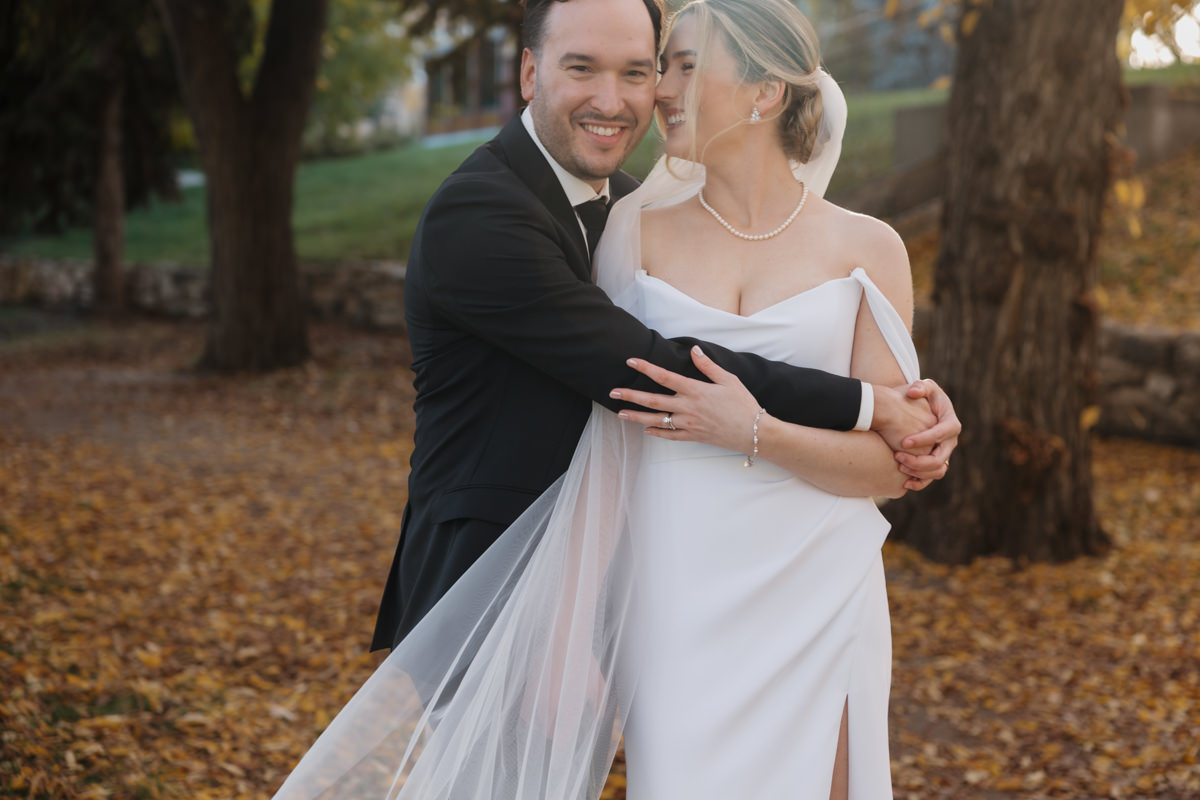 Romantic wedding portraits along Saskatoon’s scenic riverbank, with the couple framed by vibrant fall foliage