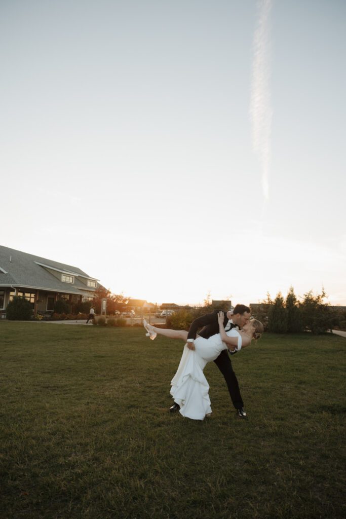Bride and groom kissing softly at golden hour with the Saskatoon skyline in the background, glowing in warm autumn light