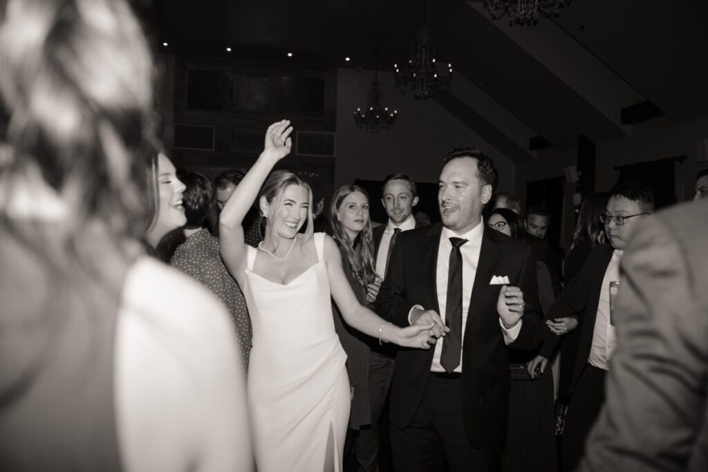 Bride throwing her hands up with joy while dancing with friends during an unforgettable wedding reception in Saskatoon.