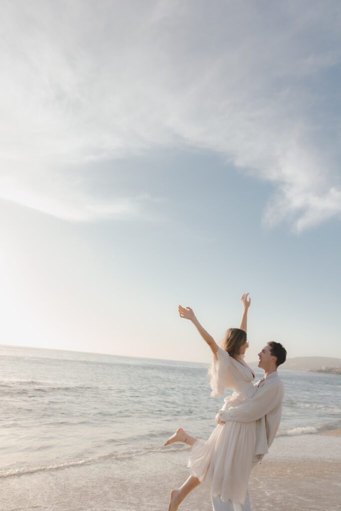 Ben lifting Lauren in front of a rocky cove at sunset