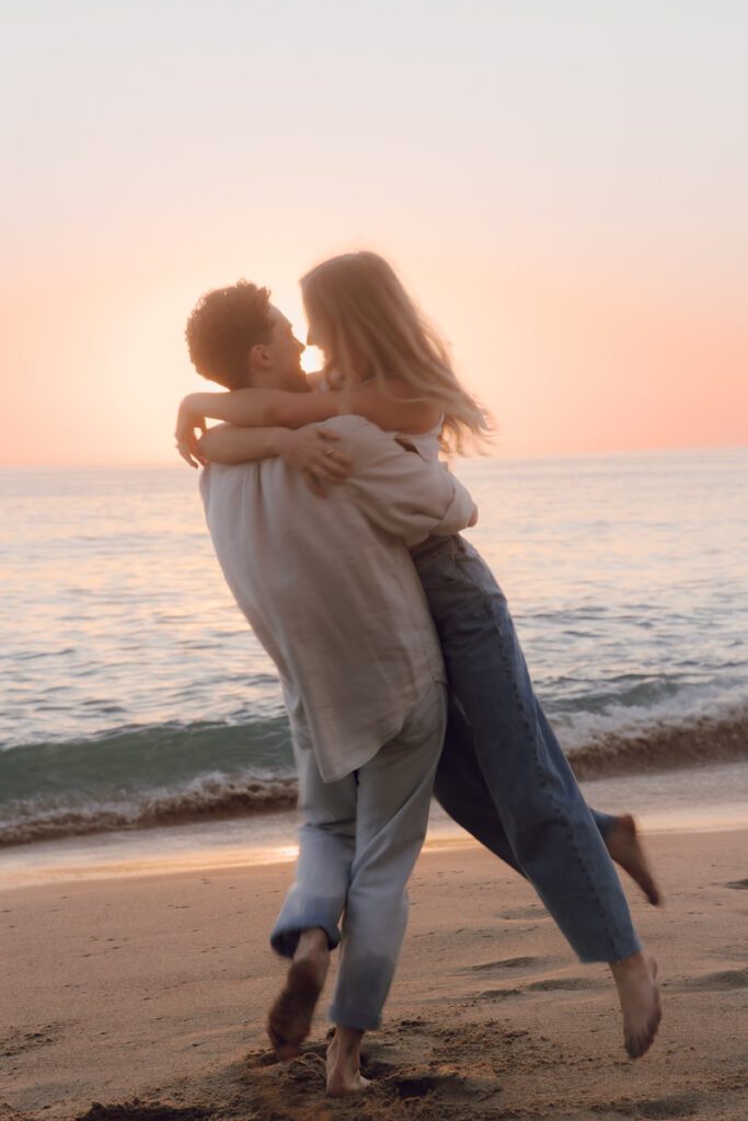 Ben lifting Lauren in front of a rocky cove at sunset