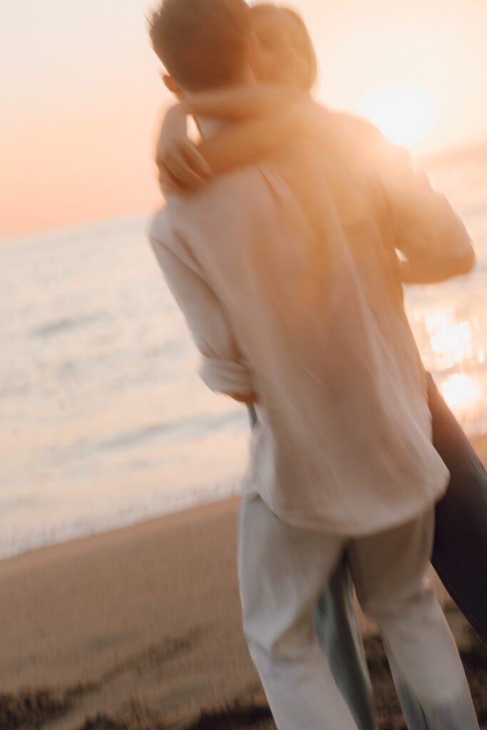 Ben lifting Lauren in front of a rocky cove at sunset