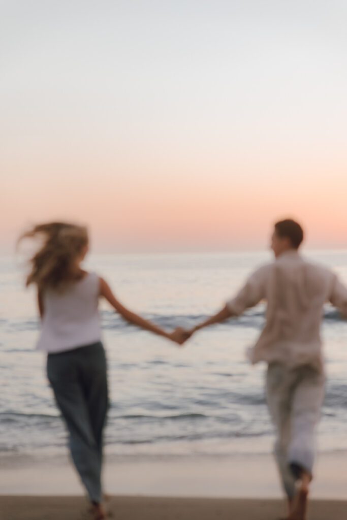 Couple laughing while walking barefoot along Laguna Beach at sunset