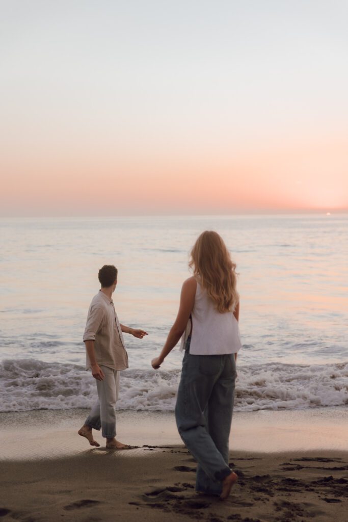 Couple laughing while walking barefoot along Laguna Beach at sunset