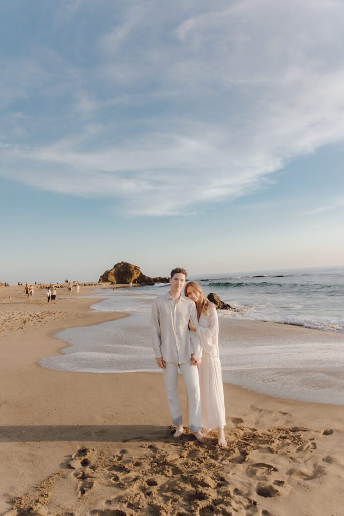 Couple laughing while walking barefoot along Laguna Beach at sunset