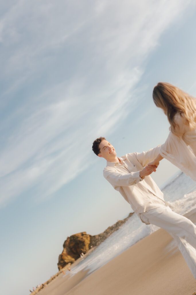 Couple laughing while walking barefoot along Laguna Beach at sunset
