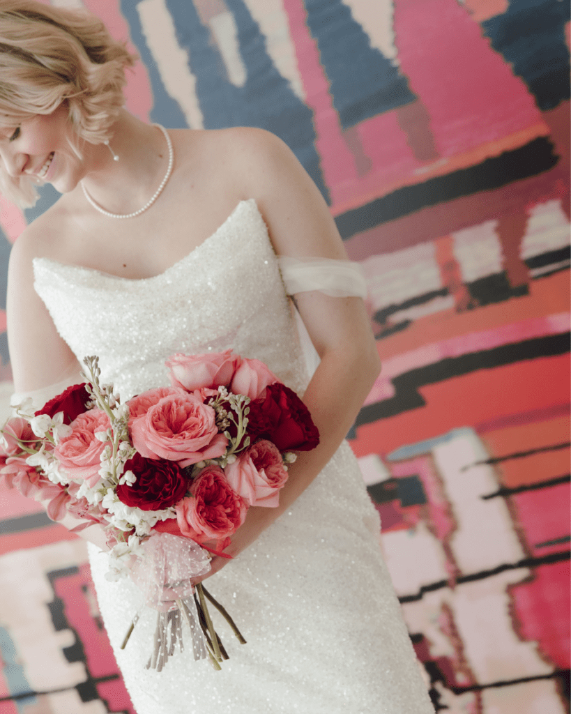 Bride in Lis Simon gown holding bouquet of red and pink flowers