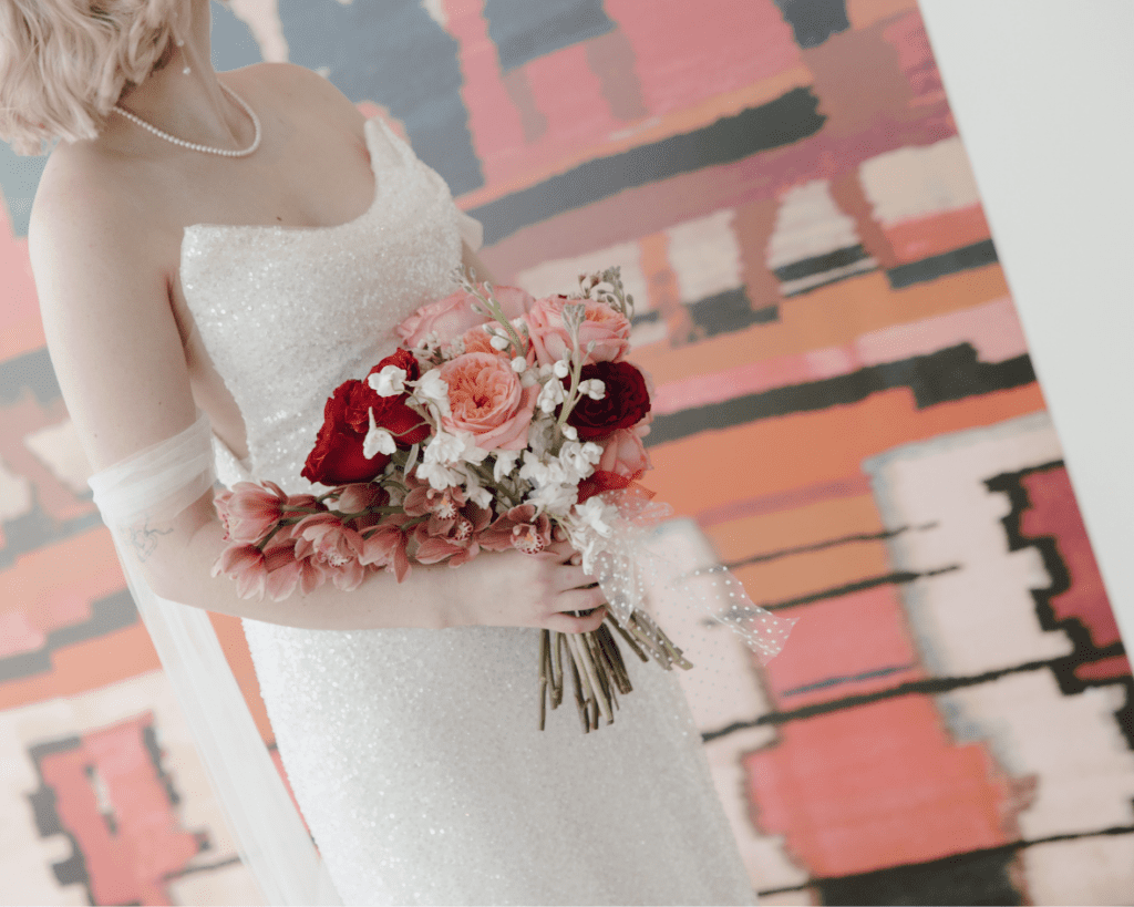 Bride in Lis Simon gown holding bouquet of red and pink flowers during her remai modern wedding