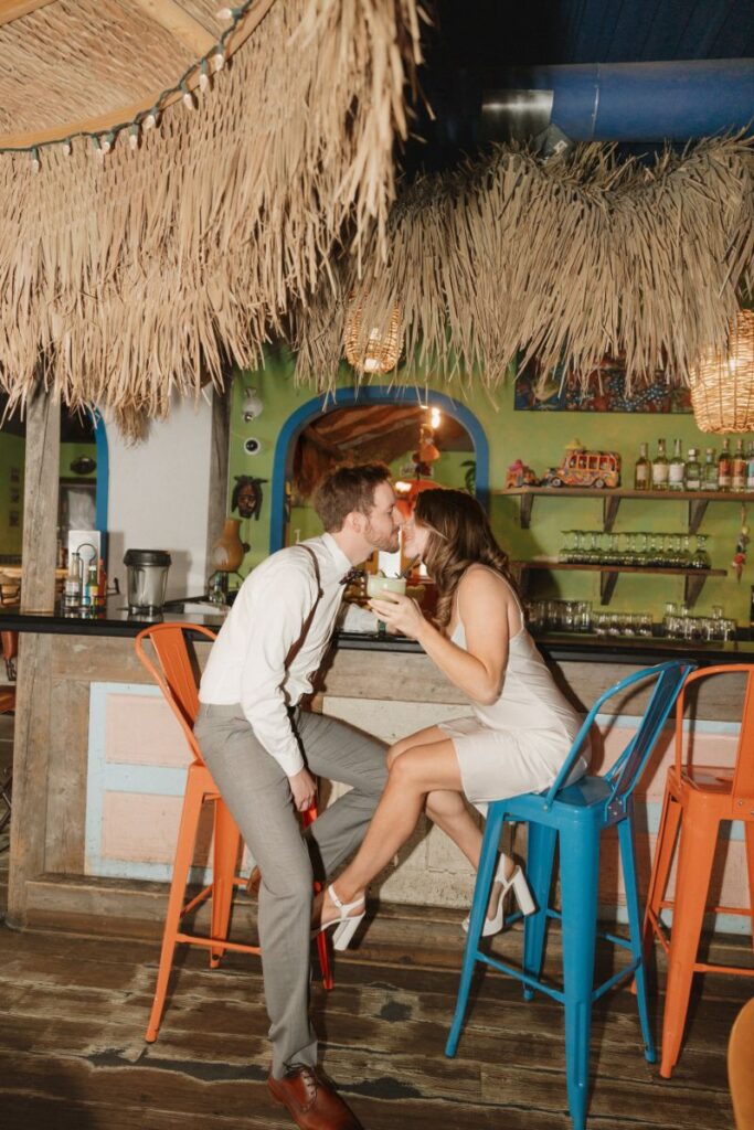 Couple smiling in front of vibrant restaurant wall with margaritas in hand