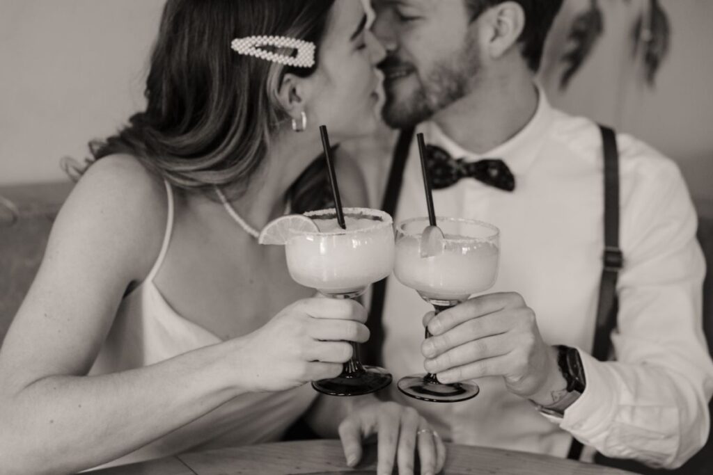 Couple smiling in front of vibrant restaurant wall with margaritas in hand
