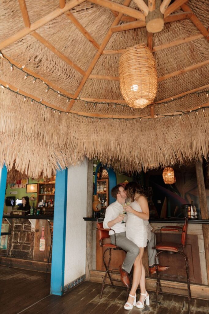 Couple smiling in front of vibrant restaurant wall with margaritas in hand