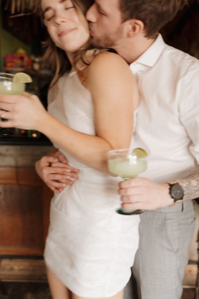 Couple smiling in front of vibrant restaurant wall with margaritas in hand
