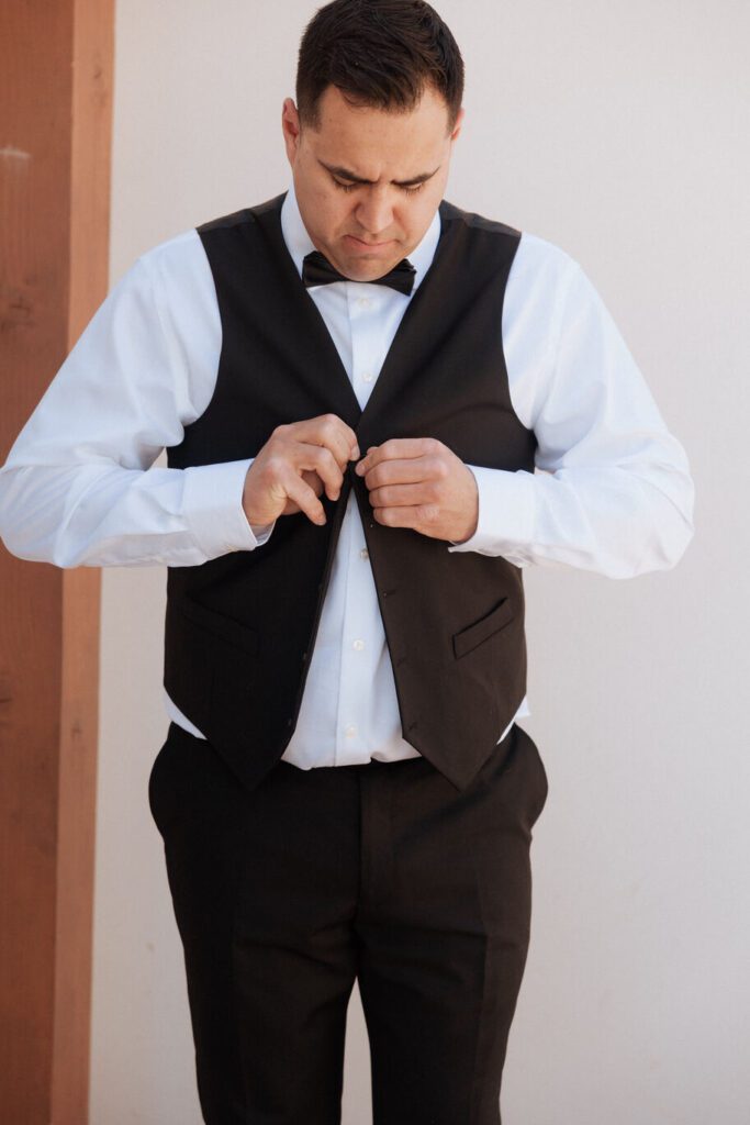 Groom adjusting tie while bride helps him get ready before elopement