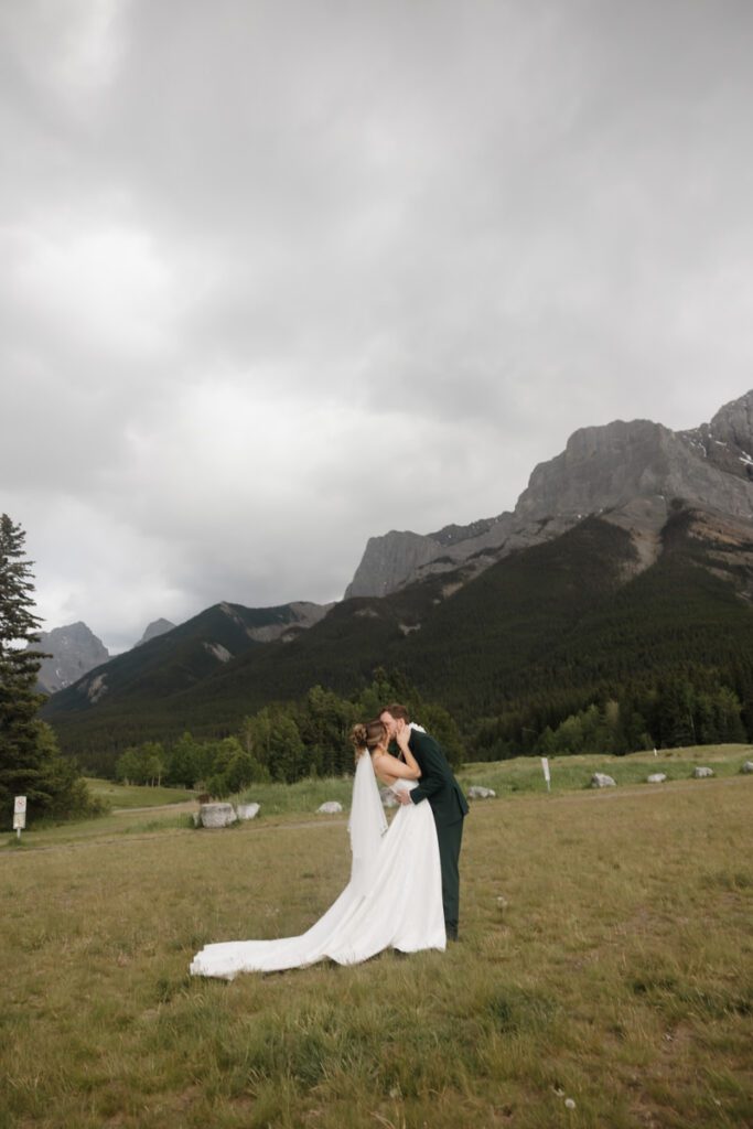 Newlyweds sharing a kiss under cloudy skies in the Canadian Rockies