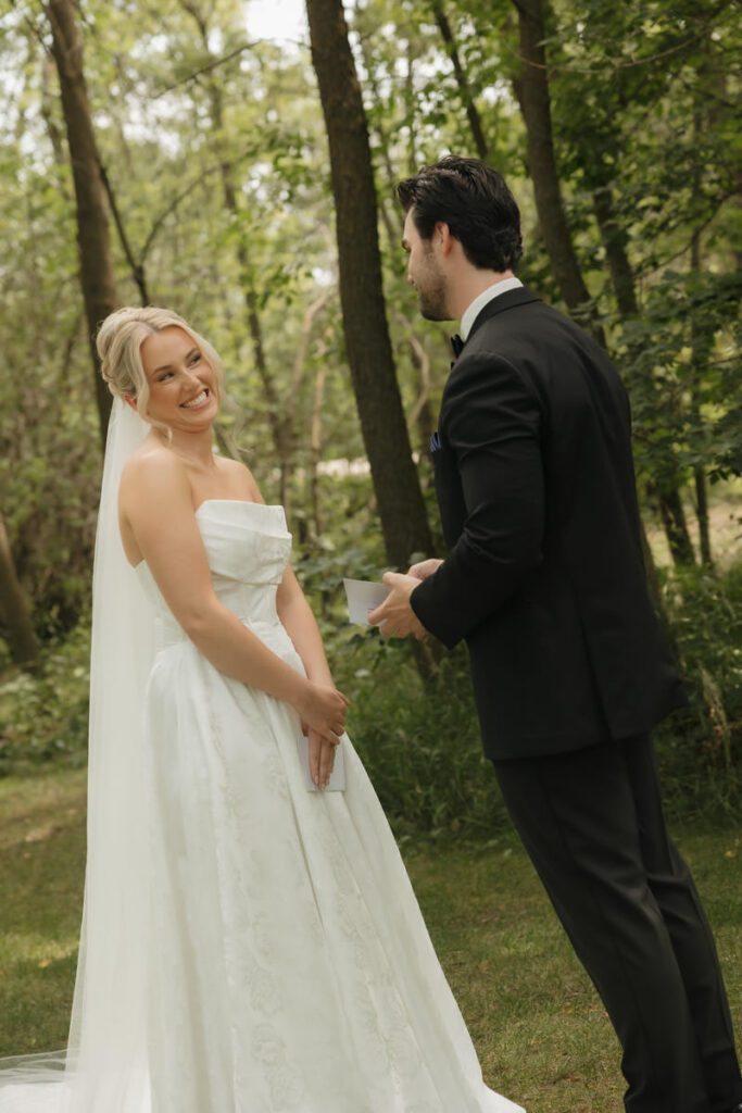 Bride laughing during vow exchange with golden light filtering through trees in moon lake wedding photography